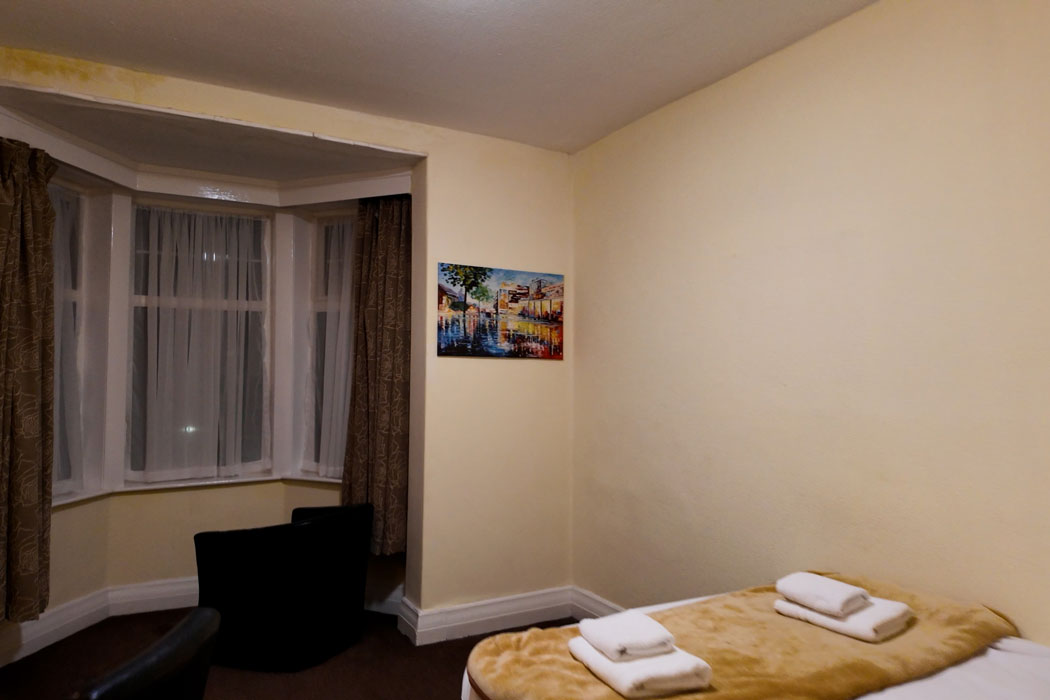 The guest rooms look dated, with net curtains, old carpet, a brown blanket on the bed and a hideous picture on the wall. The mould on the walls doesn’t improve things. (Photo © 2024 Rover Media)